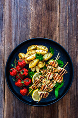 Greek style chicken skewers souvlaki with roasted potatoes and cherry tomatoes on wooden background	