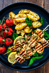 Greek style chicken skewers souvlaki with roasted potatoes and cherry tomatoes on wooden background	