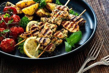 Greek style chicken skewers souvlaki with roasted potatoes and cherry tomatoes on wooden background	