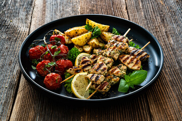 Greek style chicken skewers souvlaki with roasted potatoes and cherry tomatoes on wooden background	