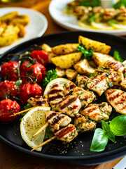 Greek style chicken skewers souvlaki with roasted potatoes and cherry tomatoes on wooden background	