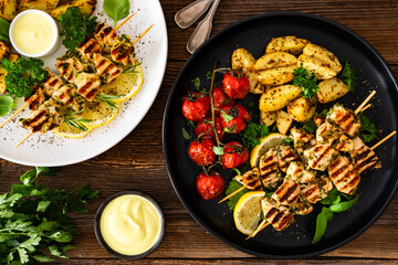 Greek style chicken skewers souvlaki with roasted potatoes and cherry tomatoes on wooden background	