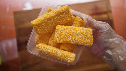 Jakarta, Indonesia 30 June 2025 : Hand holding a fried cheese roll with gooey cheese dripping....