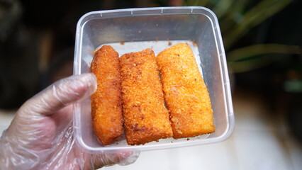 Jakarta, Indonesia 30 June 2025 : Hand holding a fried cheese roll with gooey cheese dripping....