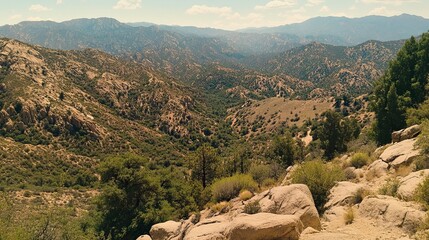Obraz premium Panoramic view of a sun-drenched mountain valley, featuring rugged terrain, sparse vegetation, and distant hazy peaks