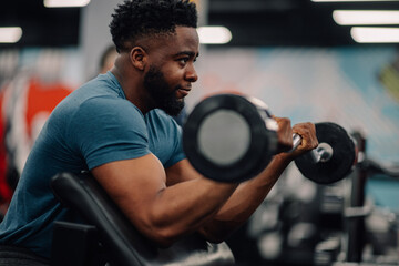 Determined bodybuilder lifting weights, concentrating on biceps exercise in gym