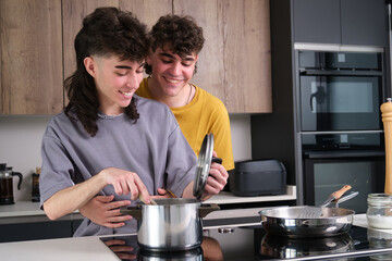 Happy couple preparing food in a domestic kitchen, stirring in a saucepan and holding the lid