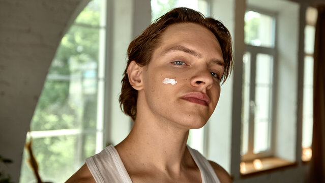 Confident young man applying skincare cream in bright modern bathroom setting