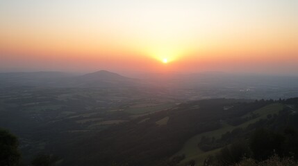 Obraz premium Serene sunset over rolling hills and distant plains, bathed in warm, golden light. A hazy atmosphere adds depth and tranquility