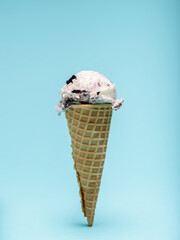 A scoop of cookies and cream ice cream atop a crispy waffle cone, against a light blue background