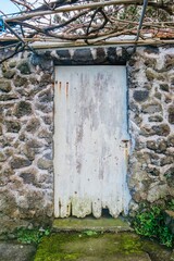 Weathered White Door Set In A Rustic Stone Wall With Overhead Vines. Abandoned Entrance, Rural...