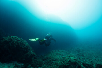 diver diving over near the seabed rocks, concept of scuba diving and underwater adventure, copy...