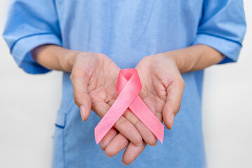 Close up asian woman breast cancer patient putting pink ribbon on hand as symbol of breast cancer...