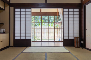 Traditional Japanese room with tatami mat flooring and sliding shoji doors opening to garden view,...