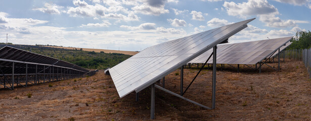 Rows of modern solar panels installed on dry, arid land under a partly cloudy sky. Represents...