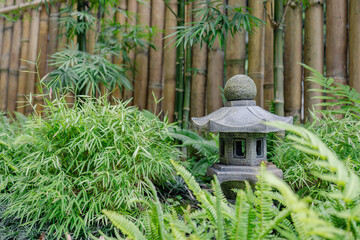 Zen garden with bamboo fence and stone lantern surrounded by green plants creating peaceful...