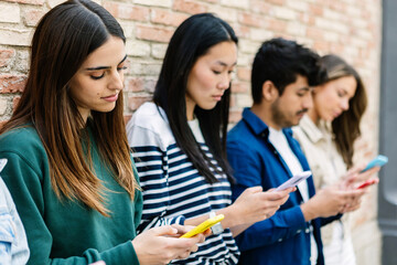 Young group of diverse people using mobile phones by brick wall. Youth and social media concept
