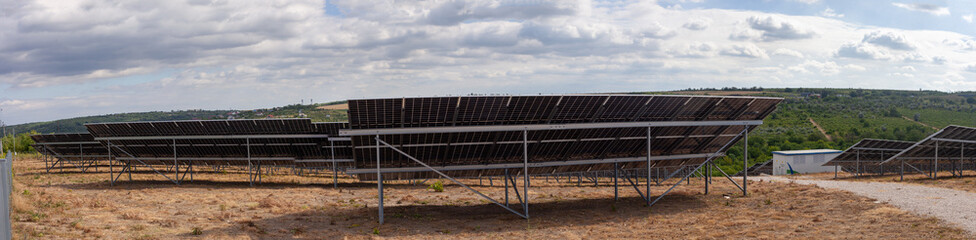 Extensive solar panel array stretches across a dry, hilly landscape under a dramatic cloudy sky....