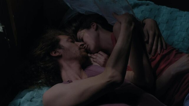 Intimate and timeless atmosphere as a couple embraces on a bed while the light changes from sunlight to shadow, with sheer tulle drifting in the breeze
