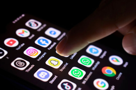 The phone screen is lit with various social media applications. The finger touches the Snapchat app, 30 June 2025, Lopburi Province, Thailand.