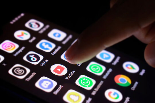 The phone screen is lit with various social media applications. The finger touches the YouTube app,30 June 2025, Lopburi Province, Thailand.