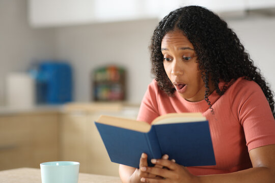 Amazed black woman reading a paper book in a kitchen