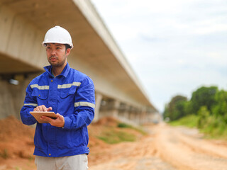 Caucasian young beautiful woman architect or builder in the hardhat standing at the roof of the building site and using tablet device, tapping and scrolling.