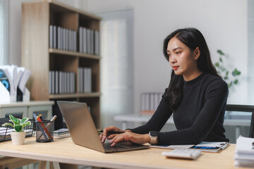 Focused asian businesswoman typing on laptop, working in modern office