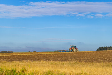 Naklejka premium Blue tractor plowing the field in Slovakia under a cloudy sky