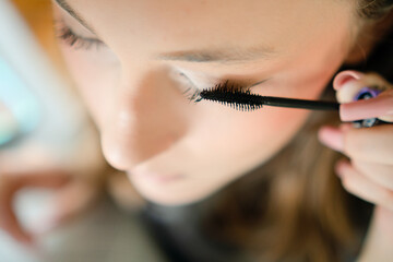 Portrait of a young teenage girl carefully applying mascara to her eyelashes. Close-up shot...