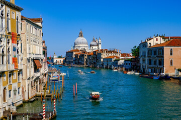 Venice Grand Canal view with boats and historic buildings under clear blue sky – panoramic perspective featuring Santa Maria della Salute and Venetian architecture in vibrant summer light