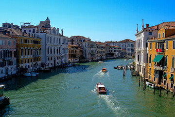 Lively Venetian canal with arched pedestrian bridge, colorful facades, waterfront caf&eacute;s and boats under a bright blue sky &ndash; authentic travel scene showcasing everyday charm of Venice&rsquo;s city life