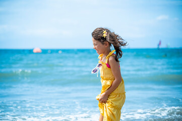 Happy Japanese girl laughing on the beach in a bright yellow dress, enjoying a summer holiday by...