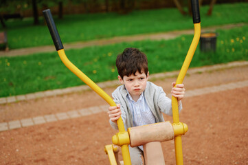 child exploring outdoor exercise equipment with curiosity and concentration. young boy gripping bright yellow handles in park setting, symbolizing childhood adventure and playfulness