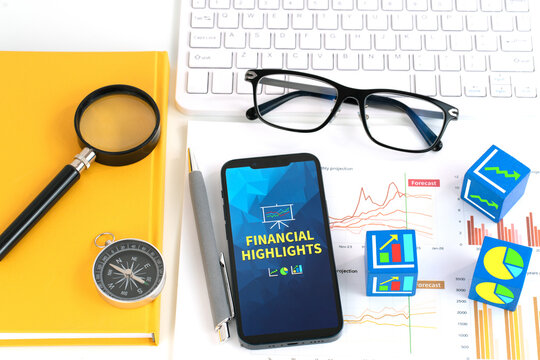 A smartphone displaying an Financial Highlights report is placed atop a stack of papers with graphs and charts accompanied by keyboard, pen, glasses, cart and magnifying glass highlighting the report