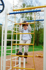 Obraz premium young boy climbing playground bars enjoying outdoor activity. child in casual clothes explores balance and strength on jungle gym, surrounded by lush greenery in park setting