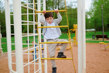 child climbing playground equipment outdoors with determination and focus. active boy wearing...