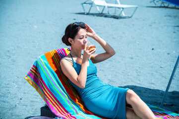 Japanese mother reclining on a colourful striped towel-covered beach lounger, smiling and enjoying...
