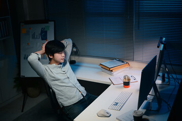 Tired male employee sits in a dark office, working overtime under dim lighting