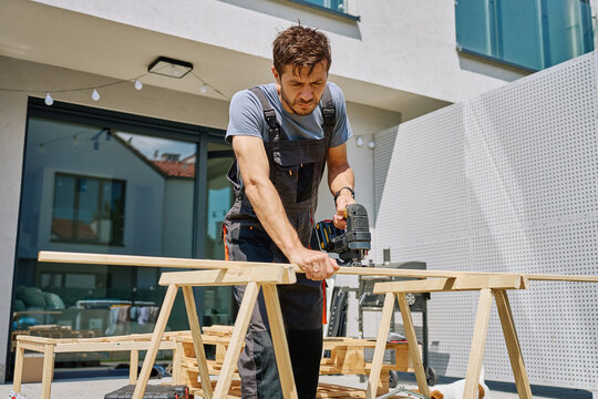Man cutting wooden plank with electric jigsaw at home backyard. Outdoor carpentry and DIY work