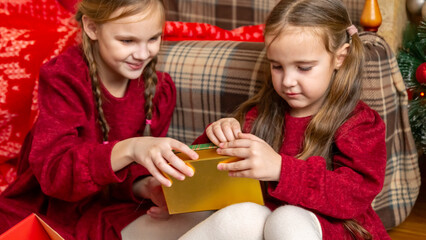 Little girls sisters open a gift box under a Christmas tree. Celebration, receiving gifts,...