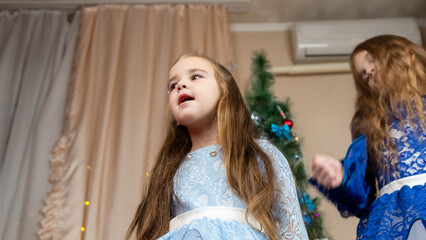Little girls in festive dress dancing near christmas tree at home