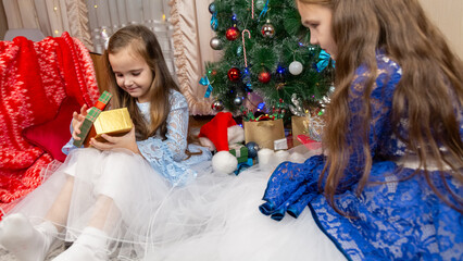 A beautiful little girls in a fluffy festive dress gets surprised with a gift in a Christmas...