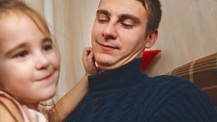 Smiling father and daughter sitting on the sofa at home near the Christmas tree