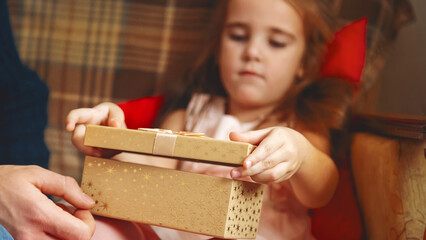 Dad is giving a gift box to his beautiful little daughter. Near the Christmas tree at home