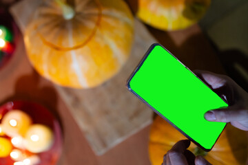 A person holds a smartphone with a green screen while surrounded by vibrant pumpkins and colorful...