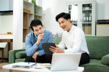 Happy Asian business partners collaborating on startup ideas using tablet and laptop in modern office.
