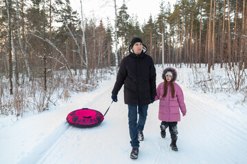 Dad with his daughter walking with snow tubing in the winter forest