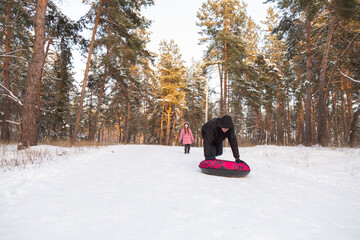 Father and daughter having fun with snow tube in the forest