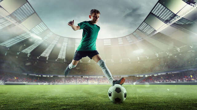 A focused boy prepares to kick a soccer ball with force on a 3D-rendered stadium field. Concept of health and fitness product advertising for kids